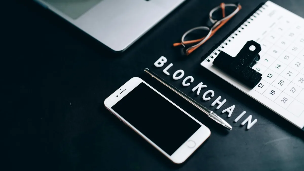 A phone, a pen and a calendar on a desk beside the word Blockchain.